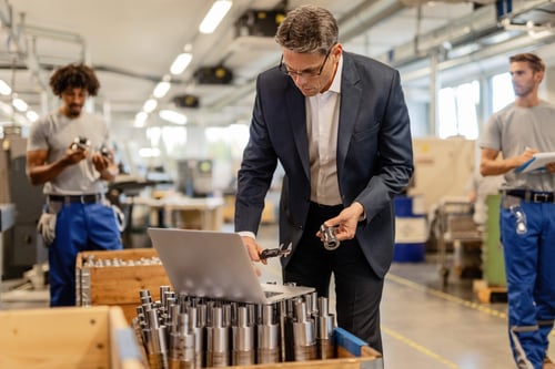 factory-manager-reading-instructions-computer-while-checking-measurements-steel-bolt-industrial-building-manual-workers-are-background-min